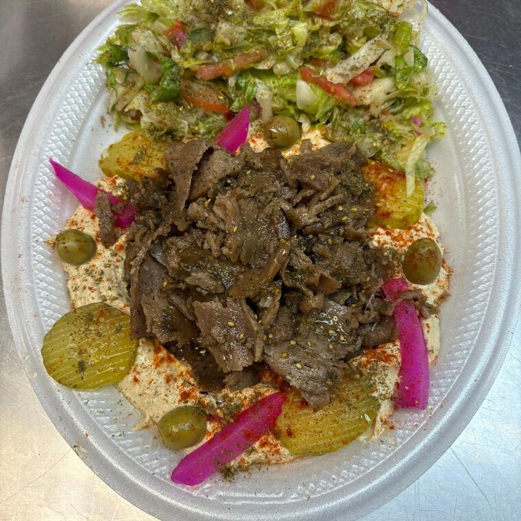 A gyro plate with pickles, olives and salad